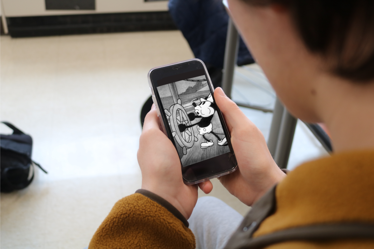 A student is looking at a photo of Mickey Mouse from Steamboat Willie. Mickey Mouse, the face of Disney, is already very popular and beloved. This iconic version of Mickey is often seen at the beginning of Disney Films, and is also very well-known. 